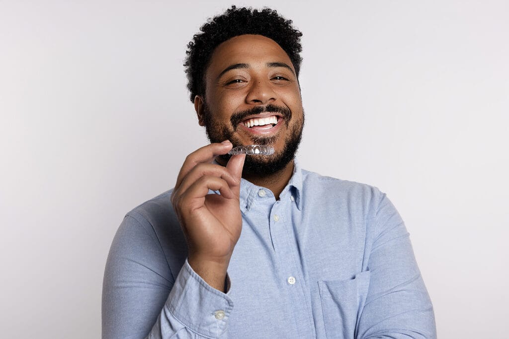 Patient smiling while holding a CandidPro clear aligner