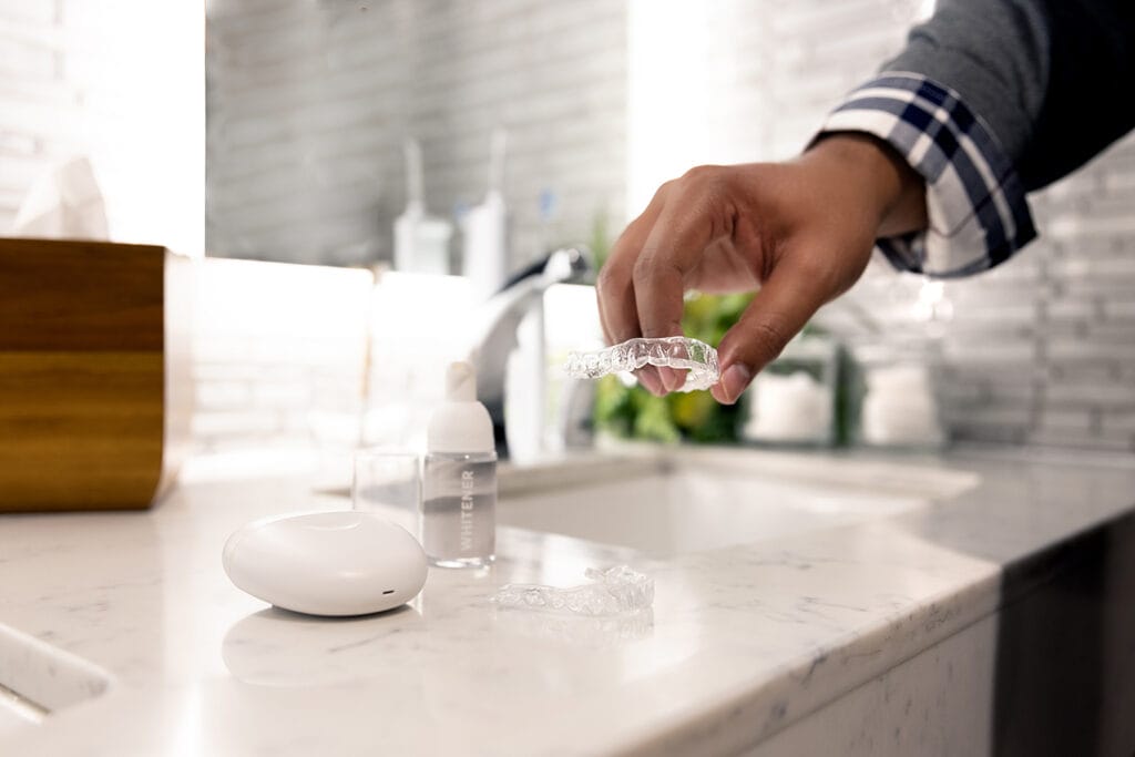 Hand picking up a clear CandidPro aligner tray from a bathroom counter